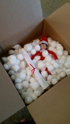 an elf in a box filled with cotton balls and a large white candle on the floor