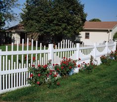 a white picket fence with red roses growing on the top and bottom, in front of a house