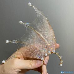 a hand holding a fake butterfly with pearls on it's wings