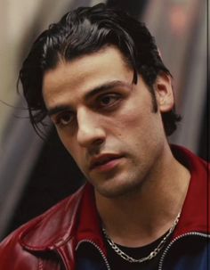 a close up of a person wearing a red jacket and black shirt with a chain around his neck