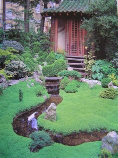 a garden with green grass and rocks in front of a small building surrounded by trees