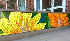 a large colorful flower painted on the side of a wall next to a sidewalk with windows