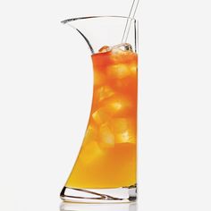 an orange drink in a tall glass pitcher with ice cubes and a straw sticking out of it