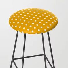 a yellow stool with white polka dots on the seat and black metal frame, against a gray background