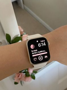 a woman's arm with an apple watch showing the time on her wrist and pink flowers in the background