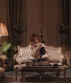 a woman sitting on top of a couch next to a table filled with chess pieces