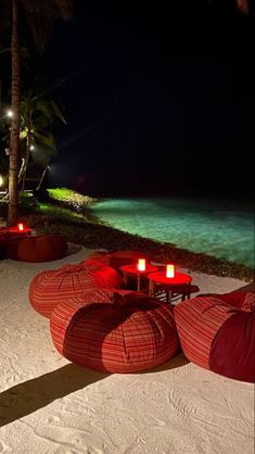 red bean bag chairs and tables on the beach at night with lit candles in the sand