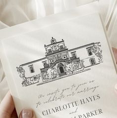 a person holding up a wedding card with an image of a building on it's front