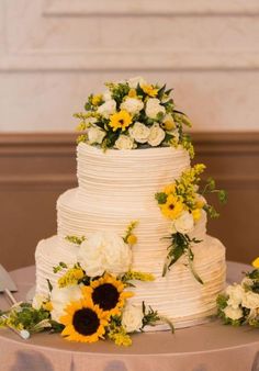 a white wedding cake with sunflowers and greenery