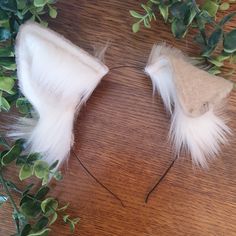 two white feathered headbands sitting on top of a wooden table next to green leaves