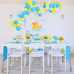 a baby shower party with blue and yellow balloons, rubber ducky decorations, and white plastic chairs