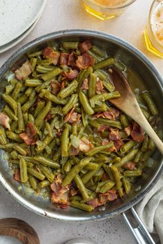 green beans and bacon cooking in a skillet with wooden spoons on the side