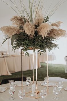 there is a tall vase filled with flowers and greenery on top of the table