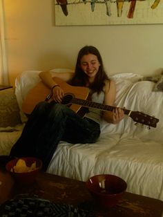 a woman sitting on top of a white couch holding an acoustic guitar in her hands