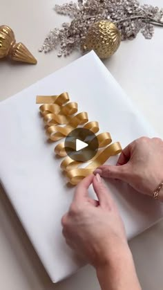 a person is cutting out gold ribbon on a white box with scissors and other decorations