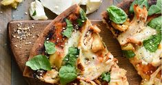 two slices of pizza on a cutting board with cheese and spinach sprinkled on top