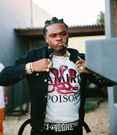 a man with dreadlocks wearing a t - shirt and black jacket standing in front of a building