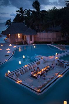 an outdoor dining area next to a pool at night with lit candles on the tables