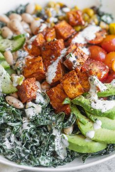 a white bowl filled with vegetables and tofu on top of spinach, chickpeas