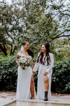 two women in white dresses standing next to each other holding hands and smiling at each other