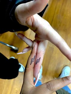 two people holding each other's fingers with lightning tattoos on their thumb and finger