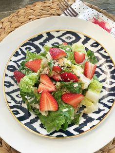 a salad with strawberries is on a blue and white plate next to a fork