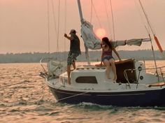 two people standing on the front of a sailboat in the middle of the ocean