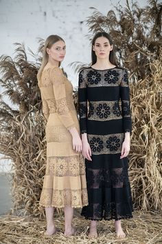 two women standing next to each other in front of dry grass and straw balks