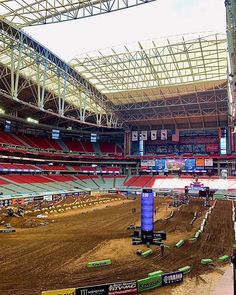 an empty stadium with dirt on the ground and people riding bikes around it, some in seats