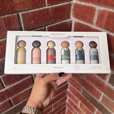 a person holding up a box with six small wooden dolls in it's packaging