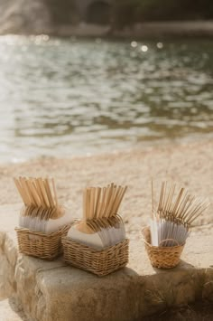 three wicker baskets with toothpicks in them sitting on the sand near water