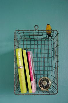 a small bird sitting on top of a wire shelf next to books and a clock