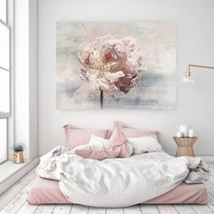 a white bed with pink pillows and blankets in front of a large painting on the wall