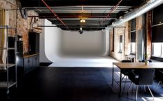 an empty room with tables and chairs in the foreground, exposed pipes on the wall