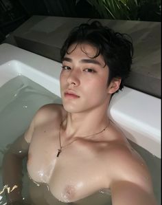 a young man in a hot tub with no shirt on, looking off to the side