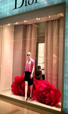 a mannequin in front of a display window with red flowers