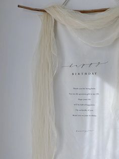 a white t - shirt with writing on it hanging from a wooden hanger next to a wall