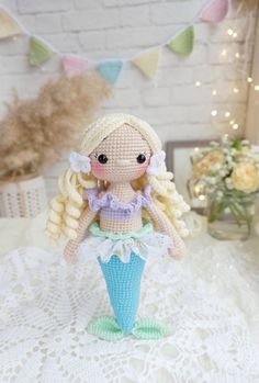 a crocheted mermaid doll sitting on top of a white doily covered table