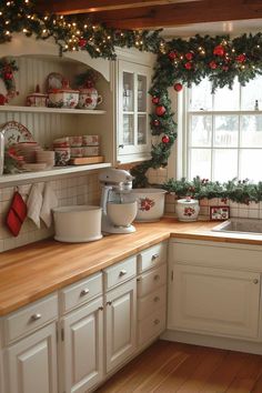 a kitchen decorated for christmas with wreaths and garland on the windowsill, white cabinets and wooden countertops