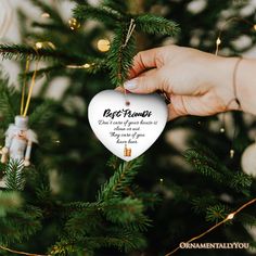 someone holding a heart shaped ornament in front of a christmas tree