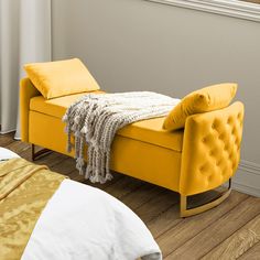 a yellow bench sitting on top of a hard wood floor next to a white bed