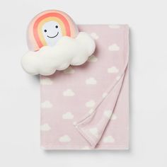 a pink blanket with a cloud and a smiling rainbow on it, sitting on top of a white surface