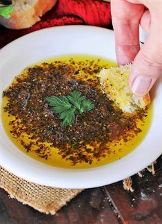 a person dipping some bread into a bowl filled with mustard and seasoning on top of it