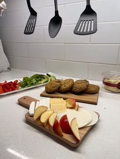 apples, cheese and cookies on cutting boards in a kitchen with utensils hanging from the ceiling