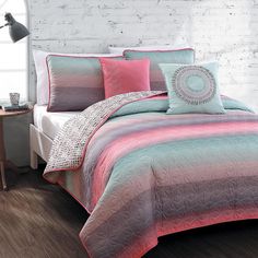 a bed with pink and blue comforters on top of it next to a night stand