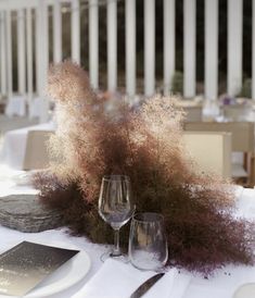 the table is set with two wine glasses and silverware, along with some purple flowers