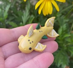 a small yellow toy giraffe sitting on top of a persons hand in front of some flowers