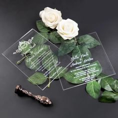 two white roses are on top of some clear acrylic cards with green leaves