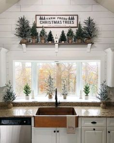 a kitchen with white cabinets and christmas trees on the window sill above the sink