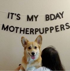 a woman holding a dog in front of a sign that says it's my bday motherpuppers